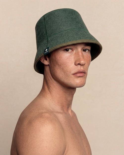 Man wearing a green sauna hat against a beige background