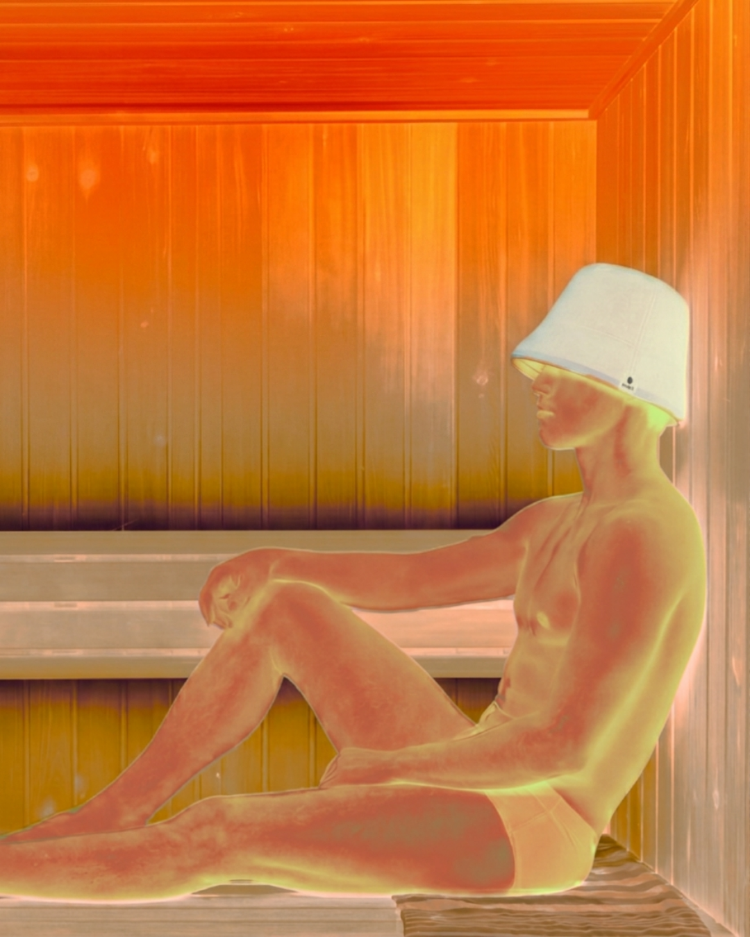 Man sitting in a sauna wearing a soft cloud Humi sauna hat with a thermal heat-map effect.